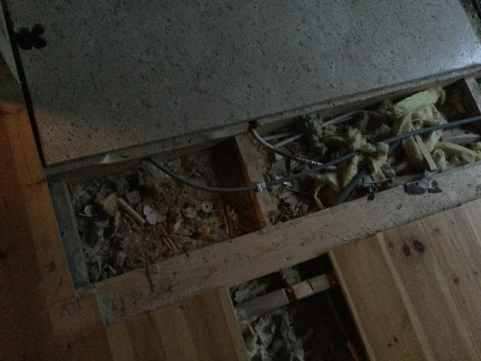 Öppet golv med isolering och kapade kablar i ett hem under renovering där ett ventilationsrör tidigare ledde till källarens badrum.