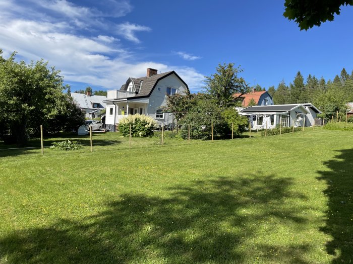 Tomt med nedbankade stolpar för stängsel i grönt gräs, med ett hus i bakgrunden.