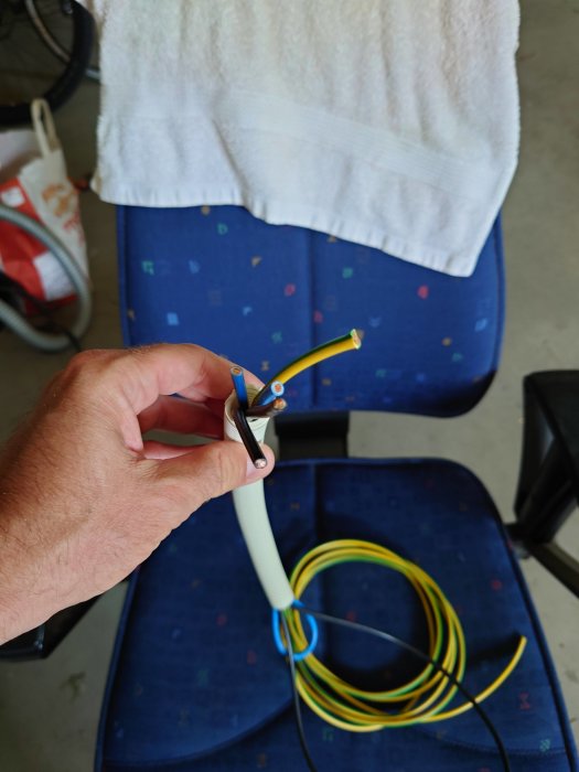 Hand som håller en elektrisk kabel inskjuten i en flexibel slang ovanför en rullad slang på stol.