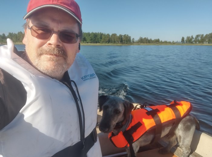Man och hund i flytvästar i en båt på vattnet i Lapplands skärgård.