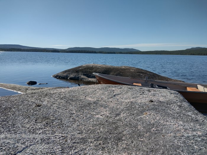 En roddbåt vid kanten av en klippig strand i Lapplands skärgård med utsikt över lugnt vatten.
