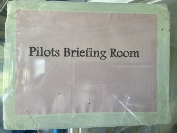Skylt med texten "Pilots Briefing Room" täckt av genomskinligt skydd och tejp på sidorna.