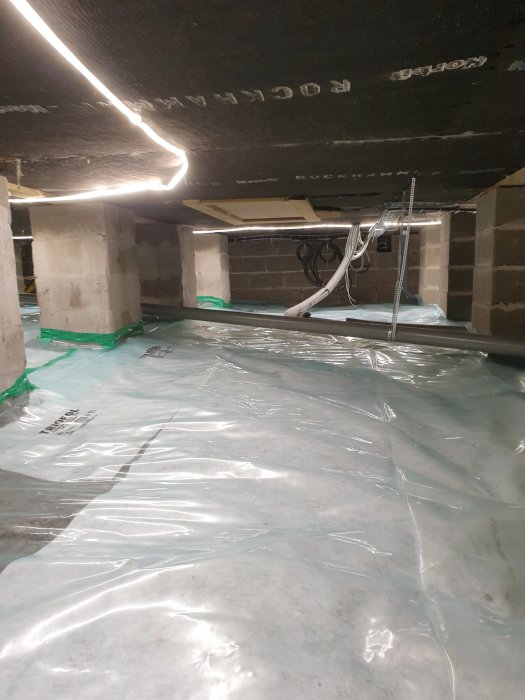 Markduk och byggplast utrullade på betonggolv med isolering ovanpå i ett källarutrymme.