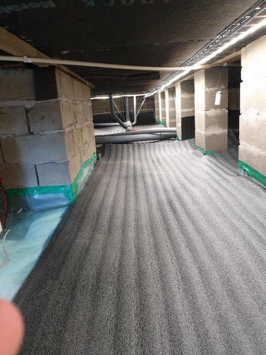 Isolerad grund med markduk, byggplast och betongtäckmatta under golvet i ett byggprojekt.