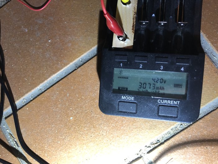 Batteriladdare med display som visar 4,20V och 3073mAh under laddning på en arbetsyta.