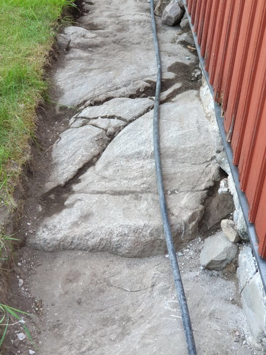 Bild på en husgrund där berget lutar nedåt, med synligt frilagt sten och murbruk.