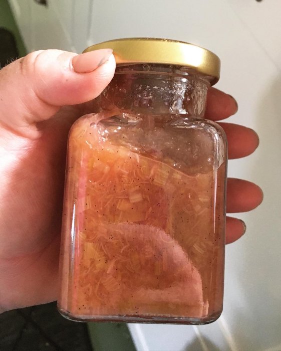 Hemgjord rabarbermarmelad i glasburk hållen av en hand.