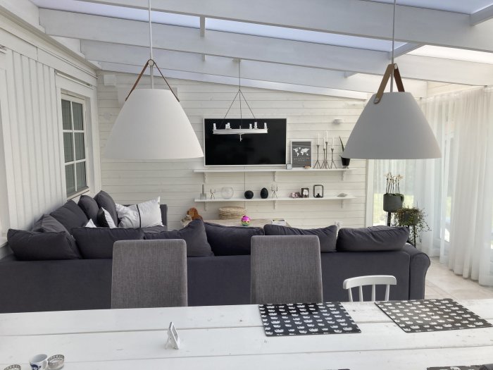 Modernt vardagsrum med stor grå soffa, vita väggar, tv-skärm och designlampor.