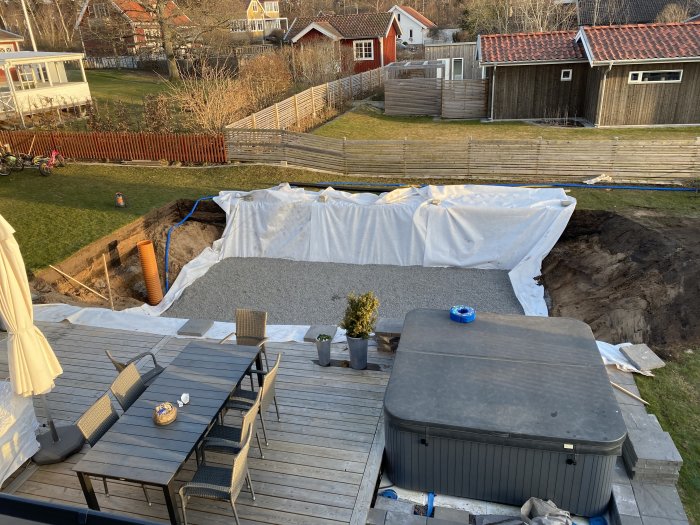 Byggprojekt av en pool i en trädgård med grävarbete och byggmaterial synliga.