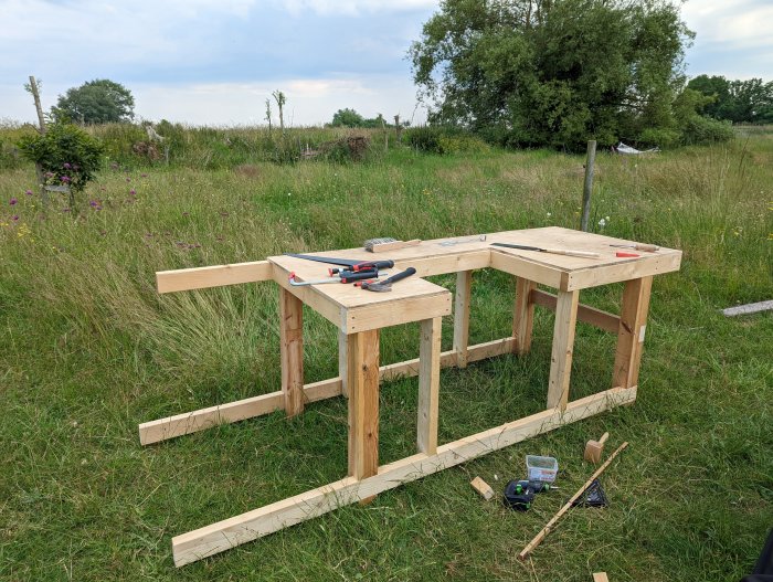 Pågående byggprojekt av träram utomhus med verktyg och material på och runt konstruktionen.