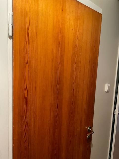 Äldre träddörr med synliga slitage och små hål som behöver slipas och behandlas, dörrhandtag i metall synligt.