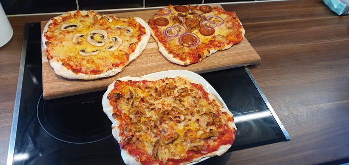 Tre hemgjorda pizzor på en träbänk, varav en med champinjoner och en med chorizo och rödlök.