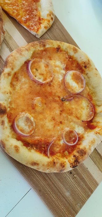 Hemgjord pizza med tomatbas och rödlök på en träskärbräda.