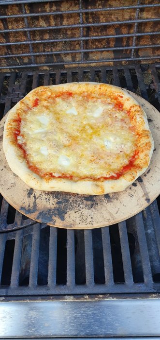 Hemlagad pizza med tomatsås och ost på en stenplatta ovanpå en grill.