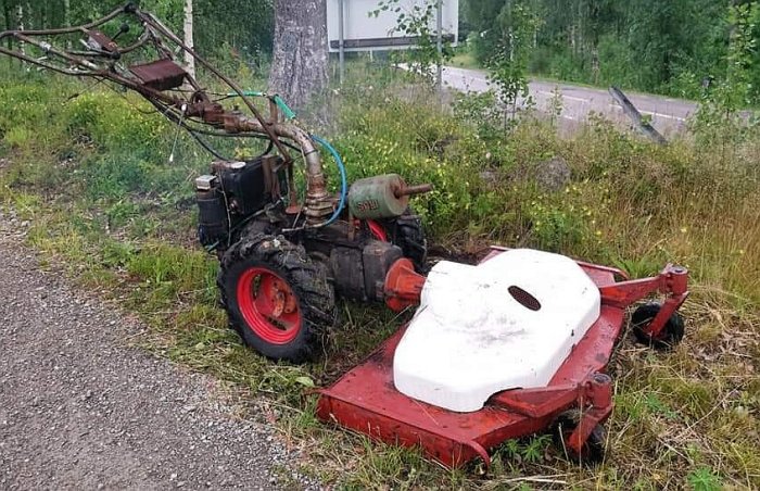 En Irus U1200K dieseldriven gräsklippare med rött klippdäck parkerad på en grusväg bredvid högt gräs.