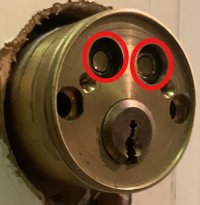 Närbild av en mässingsdörrlåskropp med markerade pluggar och insexskruv.