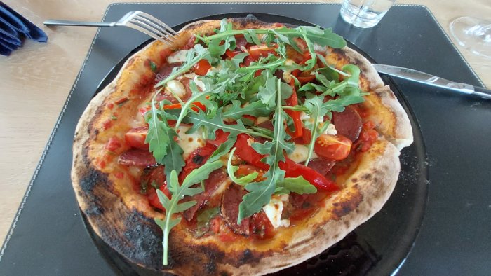 Nygräddad pizza med salami, tomat och rucola på en stenplatta, med lätta brända kanter.