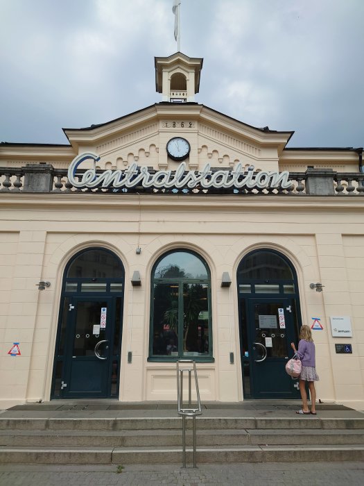 Fasaden på en tågstation med skylten "Centralstation" och en person framför ingången.