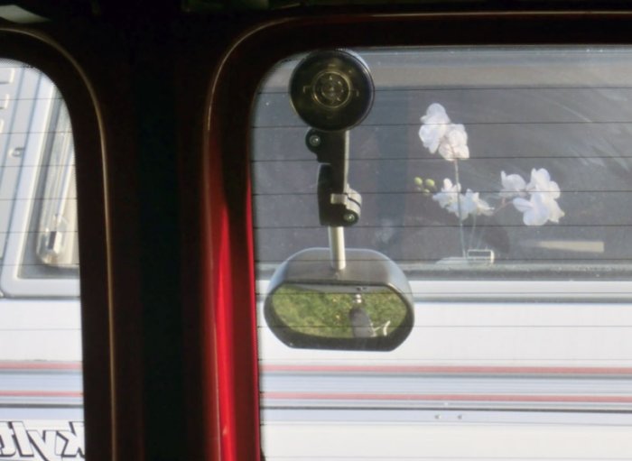 Sidospegel monterad på en bil med reflektion av blommor och landskap.