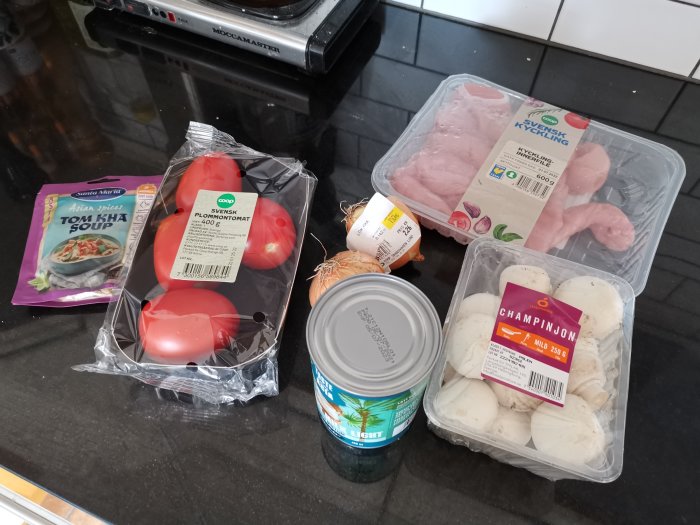 Ingredienser för Tom Kha Gai soppa på köksbänk inklusive kyckling, champinjoner, tomat och kokosmjölk.