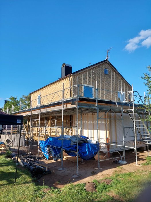 Hus under renovering med monterade ställningar och byggmaterial på gräsmattan.