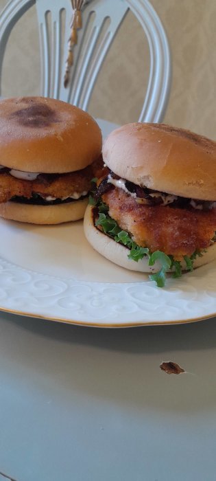 Två kycklingburgare på en tallrik med sesambröd, sallad och dressing.