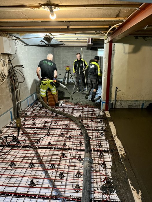 Arbetare gjuter betonggolv i källare med armeringsnät och betongslang.