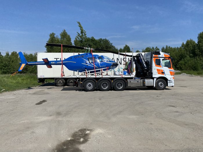 Lastbil transporterar en blå helikopter på en släpvagn utomhus.