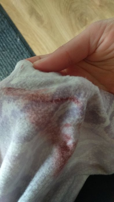 Hand håller en tygbit med röd färgfläck som kan vara färg eller fläck från byggprojekt.