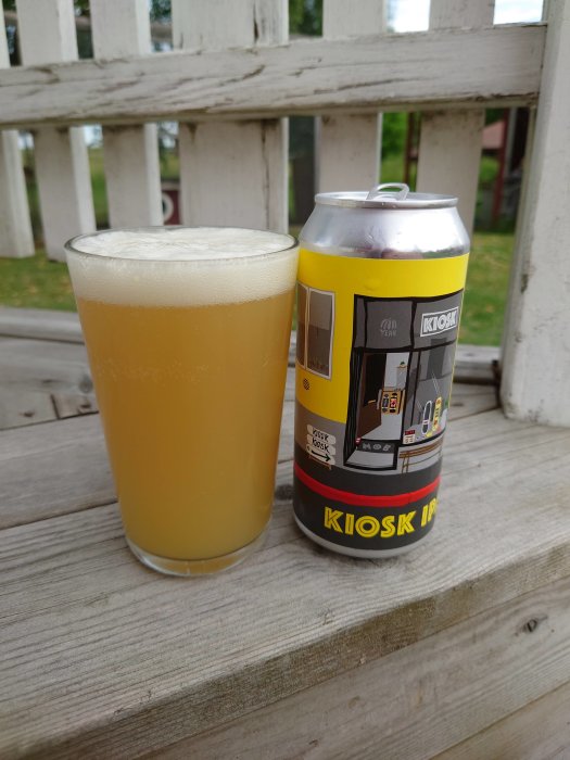 Ett glas med öl bredvid en burk märkt "KIOSK IPA" på ett trätrappsteg.