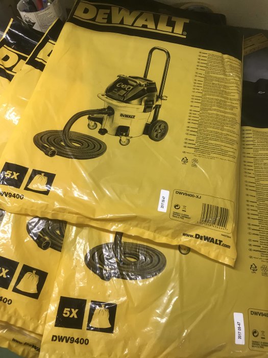 Stapel med DeWalt dammsugarpåsar, DWV9400-XJ 5-pack, i förpackningar.