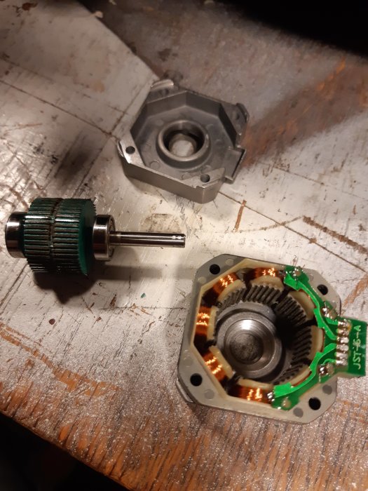 Demonterad elektrisk motor med rotorn, statorn och motorhöljet separat på ett slitet träbord.