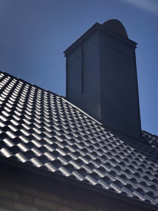 Nyinplåtad skorsten på svart tegeltak under solig himmel, med synliga ojämnheter på plåtarbetet.