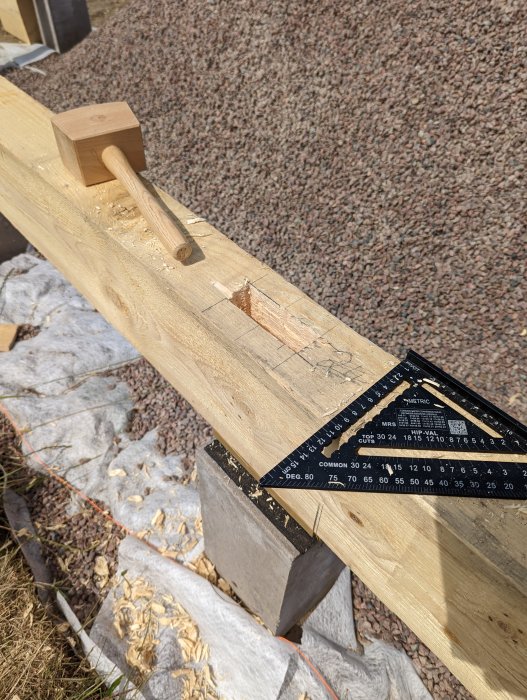 Träbjälke med hammare, träspån och tappmått, mätning för sammanfogning på byggarbetsplats.