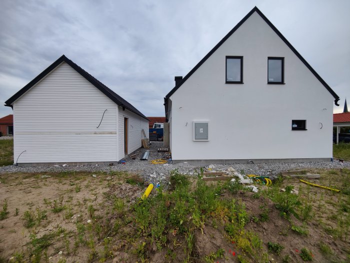 Nybyggt hus med fasad och knack avslutat, garageport och solpaneler monterade, byggmaterial på marken.