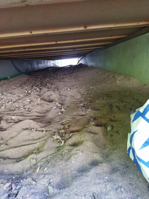 Vy under fritidshus som visar plintgrund, längsgående balkar och ojämnt underlag.