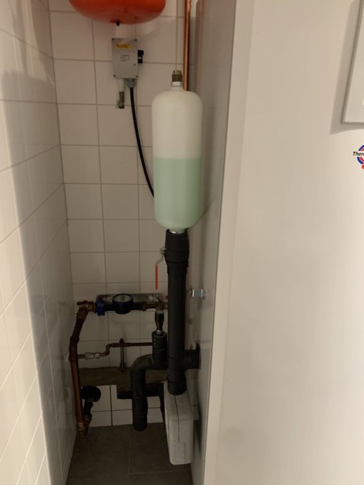 Rörsystem och expansionskärl bredvid en bergvärmepump med synlig fukt i tvättstuga.