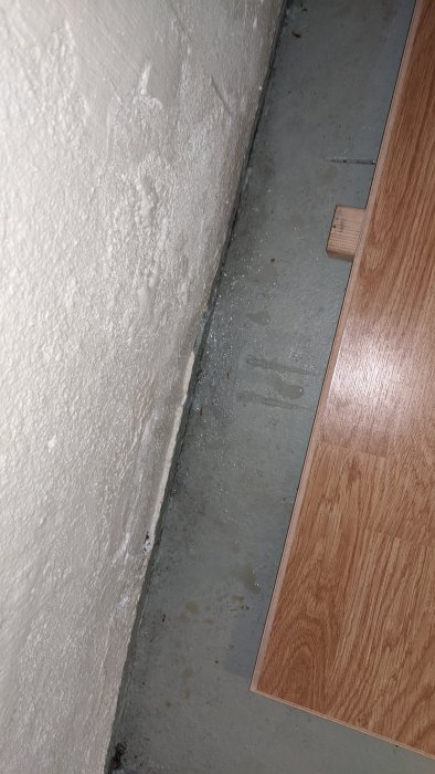 Källarhörn med synlig fuktskada och vattendroppar längs väggen och på betonggolvet.