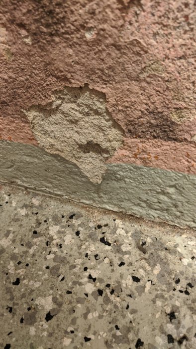 Skadad källarvägg med avfallande puts ovanför ett kallt betonggolv med fuktskador.
