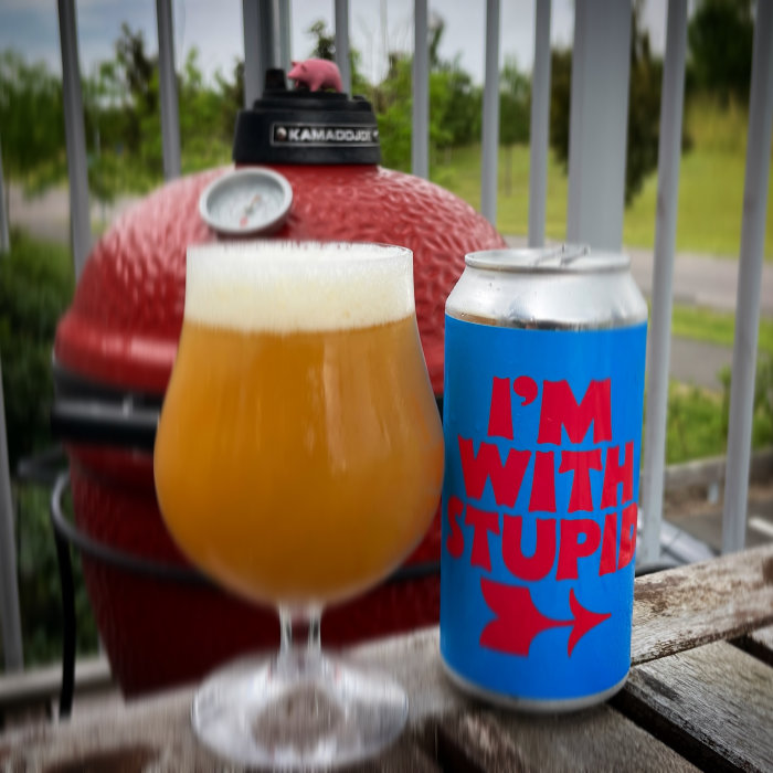 Ett glas öl och en burk med texten "I'M WITH STUPID" framför en röd grill.