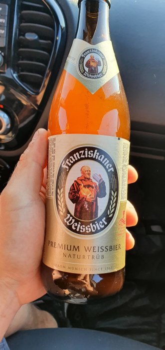 Flaska Franziskaner Weissbier hållen i hand framför bilratt.