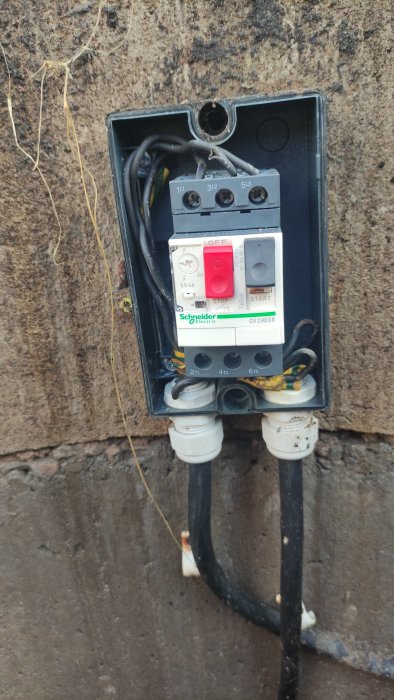 Elektriskt kapslad 3-fas vattenpumpsmotorskydd med avstängd strömbrytare monterad på en betongvägg.