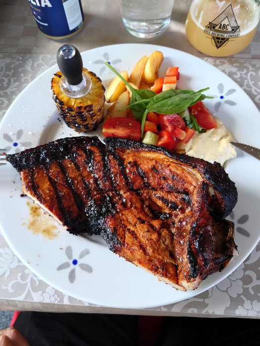 Grillat kött med grillmönster på tallrik med potatis, grönsaker och ölglas på sidan.