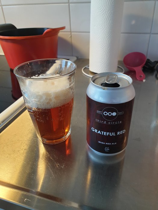 Glas med röd ale och en burk öl märkt "Grateful Red" på ett köksbänk.