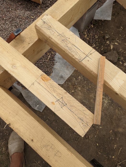 Utskurna ändar av två träbalkar förberedda för att skarvas ihop, med uppritade linjer och en hammare i bakgrunden.