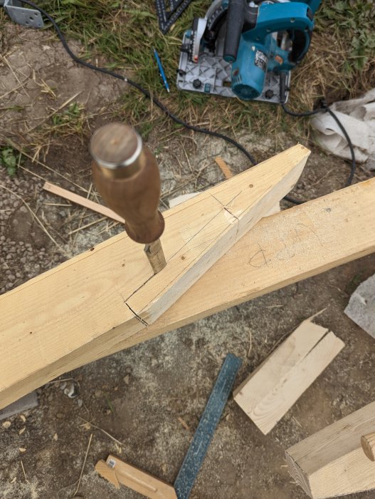 Hantverk av en hammarbandsskarv med markerade snittytor och stämjärn på ett trästock i en byggmiljö.