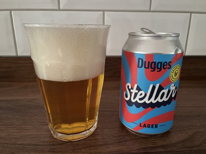 Ett glas öl bredvid en färgglad burk med texten 'Dugges Stellar Lager' på en köksbänk.