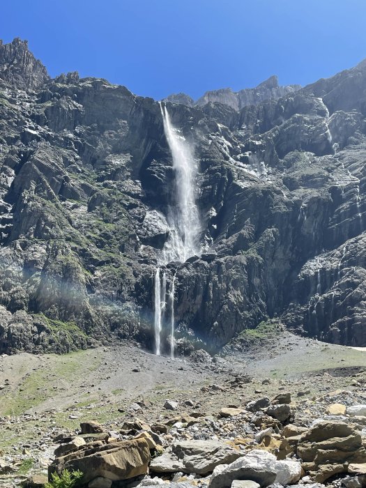 Vattenfall i bergslandskap med klippor och blå himmel.