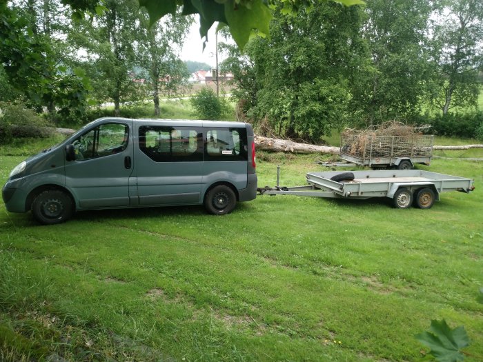 Grå personbil kopplad till tom släpvagn och en annan vagn fylld med grenar.