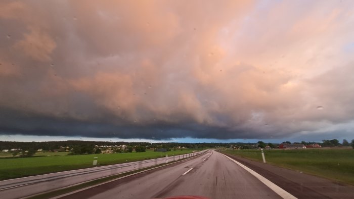 Vy från bilkörs perspektiv på motorväg under dramatisk himmel med mörka moln.